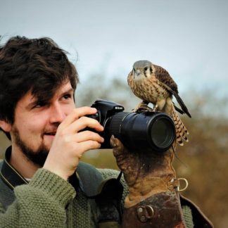 Man with bird sitting on his camera at The Falconry School
